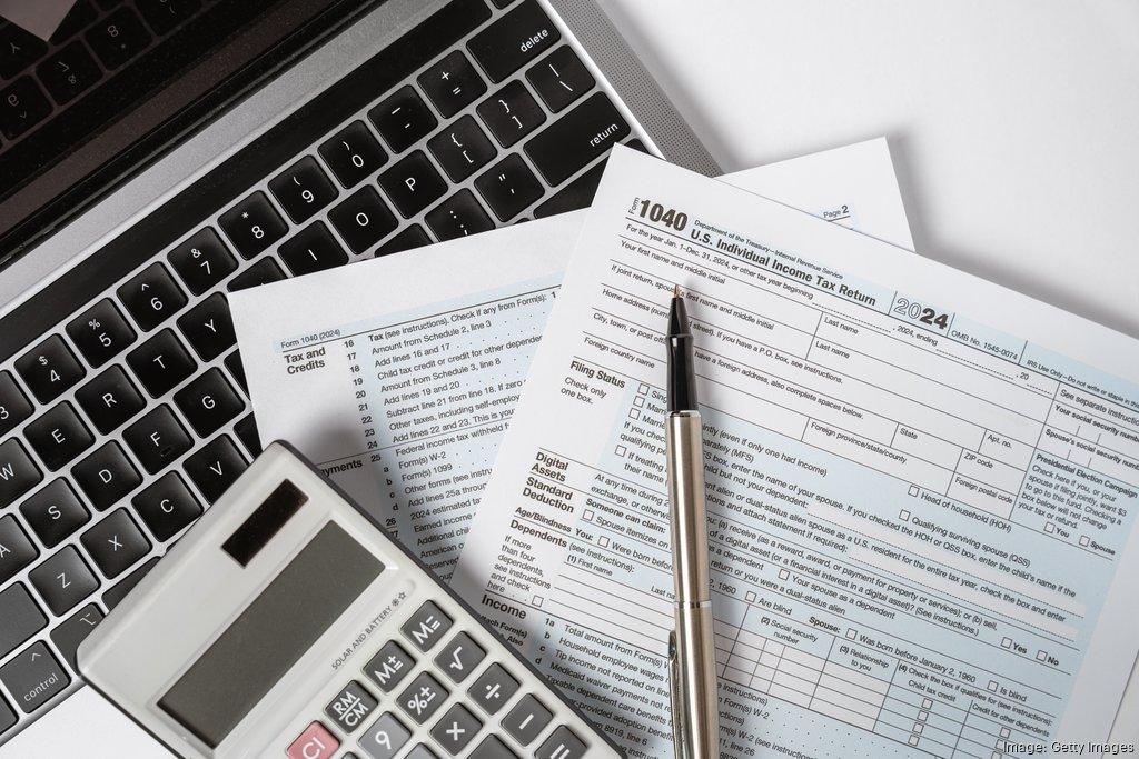 Tax documents and calculator resting on a laptop keyboard, ready for filing U.S. Individual Income Tax Return