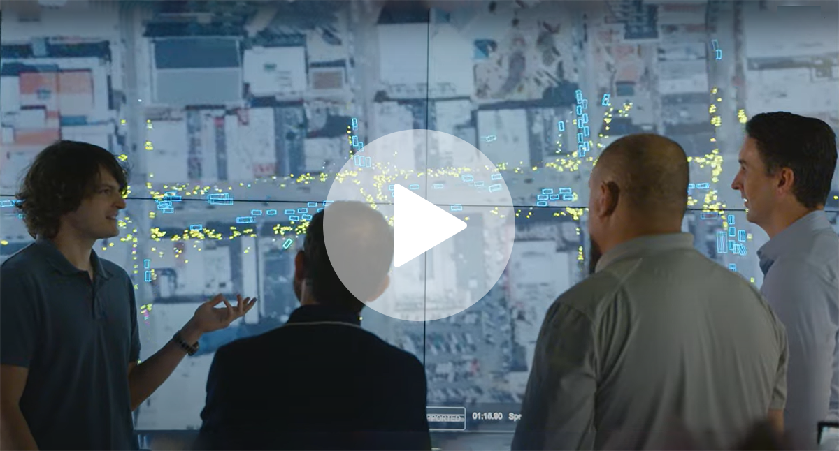 ChatGPT said: Four people discuss data visualization displayed on a large screen showing a city map with highlighted yellow and blue markers.