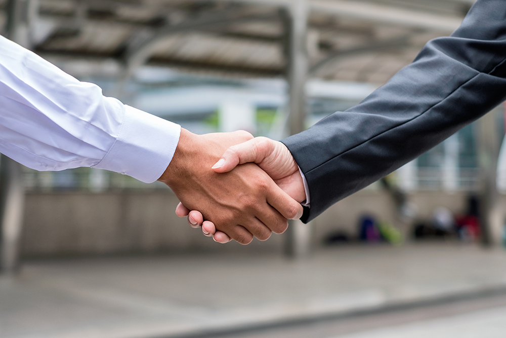 A close-up of two people shaking hands under dramatic blue lighting, signifying collaboration and agreement.