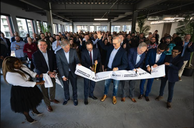 Leaders and partners cut a ceremonial ribbon as a large crowd gathers inside a modern office space.
