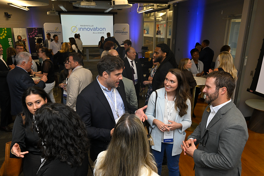 Professionals networking and talking in a conference space during an innovation event, with presentation screens and groups conversing throughout the room.