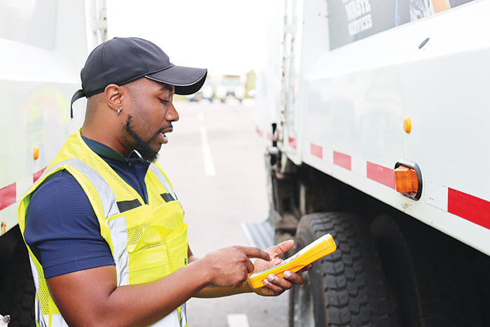 Information System Application Tech Mike Brown uses a handheld device beside a truck in an outdoor service area to complete a post-trip inspection on a fleet vehicle.