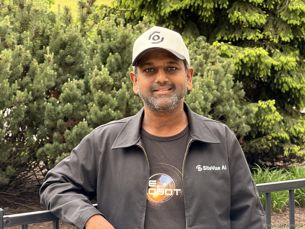 Andrew Jebasingh, founder and CEO of SiteVue, stands outdoors in front of evergreen trees, wearing company-branded apparel.